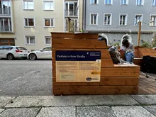 Das Schild "Dein eigenes Parklet" auf einer Holzwand.