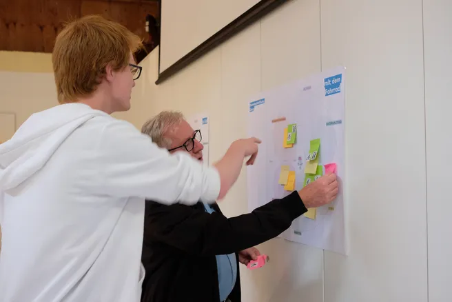 Two people are putting Post-Its on a wall.