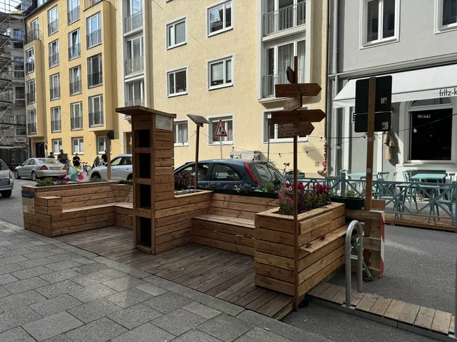 A Parklet in Steinheilstraße, which proivdes benches, bicycle parking, a sign, plants, and a swap shelf.