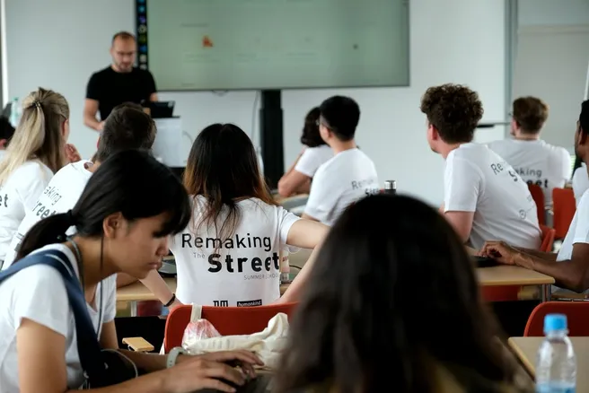 Students are sitting in a class room and wearing T-Shirts with the term "Reamking the Street summer school 2024"